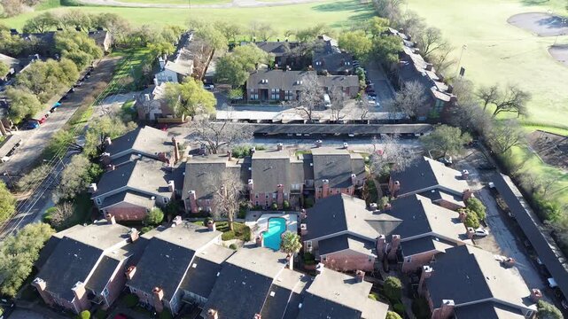 Courtyard pool enclave near Fair Oaks Ave and Holly Hill Dr highlights semicircular apartment layout surrounding pool beside open athletic fields. Dark roofs, brick walls, soft greenery, Dallas