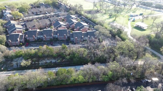 Rail&ndash;park edge view near Fair Oaks Ave and the SoPac Trail captures townhomes bordering wooded buffer and active park space with paths and play areas. Brick facades, dense trees, midtown Dallas