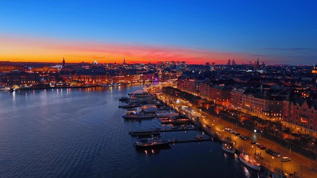 Beautiful illuminated quay with boats standing along, long promenade and highway, lined with park. Fantastic lights of Stockholm, Sweden in the evening. Aerial view.