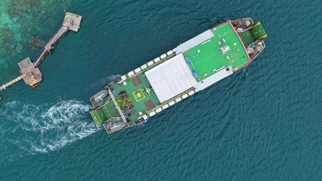 Aerial view of a ferry leaving Karimunjawa ferry harbour, creating a white foamy wake in the blue sea, Karimunjawa, Central Java, Indonesia.