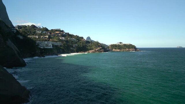 Joatinga beach and luxury houses on shore cliffs during a clear morning in 4K Apple ProRes 422. Forward aerial over the ocean.
