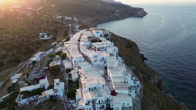 Wide cinematic drone footage flying over the historic Kastro village in Sifnos Greece during a golden sunset showing traditional white houses on a rocky cliff with the Aegean sea in the background
