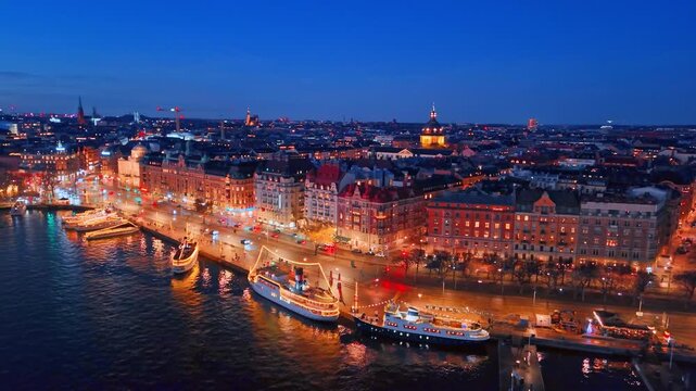 Beautiful boats decorated with lights stand near the waterfront. Aerial view on the gorgeous historical buildings of Stockholm, Sweden in the evening.