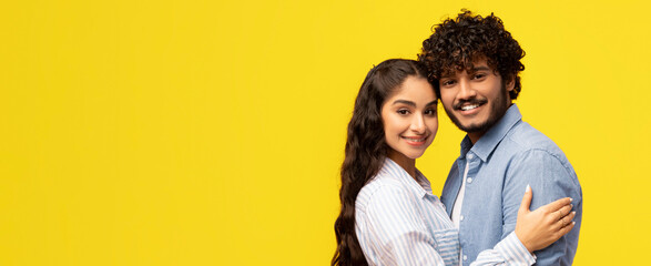 Fototapeta premium Two friends smile and pose closely together, enjoying a moment of happiness. They stand against a bright yellow background, showing their friendship and joy.