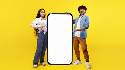 Two individuals stand in front of a large phone with a blank screen. The background is bright...