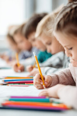 Education training class. Knowledge learning improvement study. A group of children sitting at a table, each holding a pencil and drawing on a piece of paper.