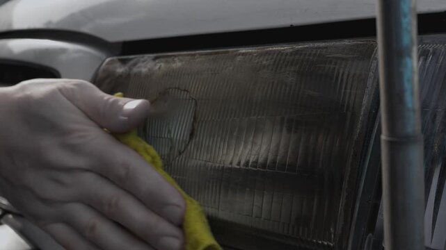 Wiping the front headlight of an old car from dirt and dust with a damp cloth, close-up
