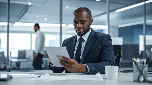 A formally dressed man in a suit looks at a tablet while seated in a modern office
