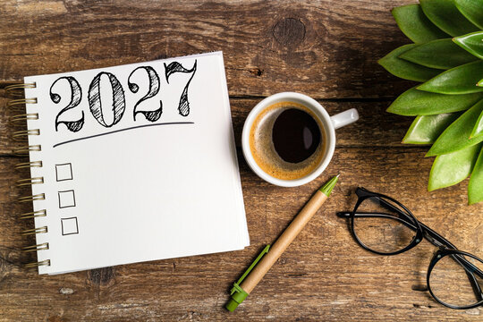 New year resolutions 2027 on desk. 2027 goals list with notebook, coffee cup, plant on wooden table. Resolutions, plan, goals, action, checklist, idea concept. New Year 2027 template, copy space