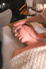 Facial massage session in cozy spa, esthetician caring for relaxed woman on treatment bed, skincare wellness ritual, aromatherapy candlelight, self care, mirror reflection.