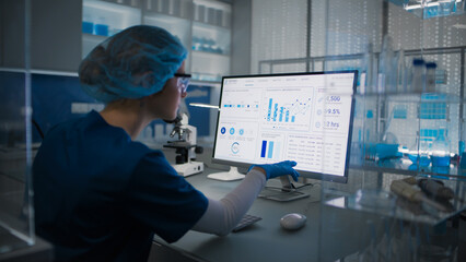 Female scientist in protective clothes and glasses looking at the computer screen. Researching human genetic diseases and DNA test results © Marcin Janiec