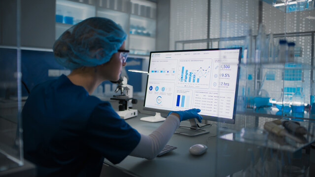 Female scientist in protective clothes and glasses looking at the computer screen. Researching human genetic diseases and DNA test results