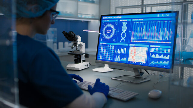 Female scientist in protective clothes and glasses looking at the computer screen. Researching diseases and DNA test results