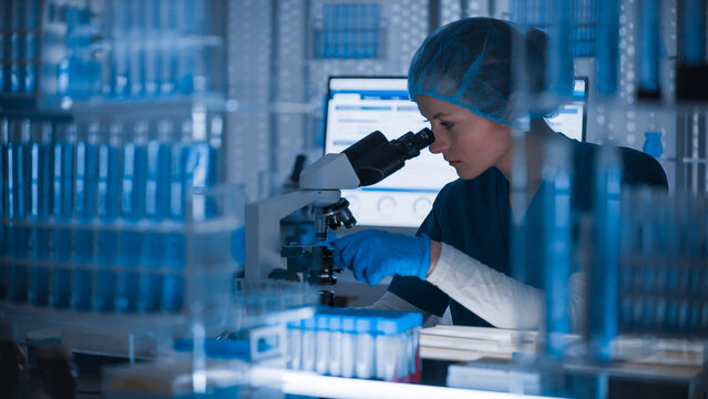 Female researcher in protective wear examining samples and vials. Medical testing