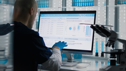Male researcher or a doctor examining test samples and comparing to the data on a computer