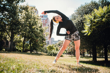 Naklejka premium Young woman outdoors stretching in the park during a sunny day workout and wellness session