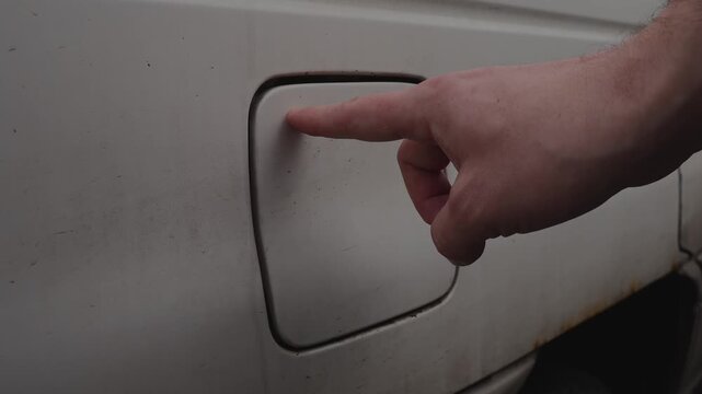 A close-up of a hand closing the fuel flap on an old car