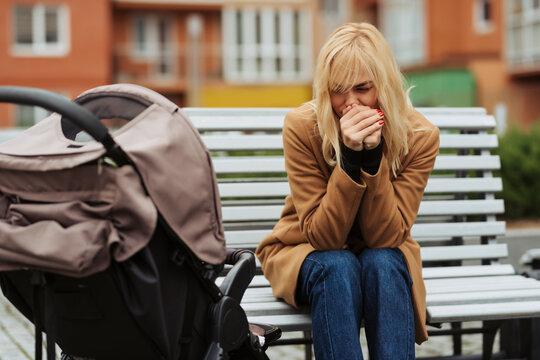 Worried young mother sitting on a bench next to a stroller in an urban park