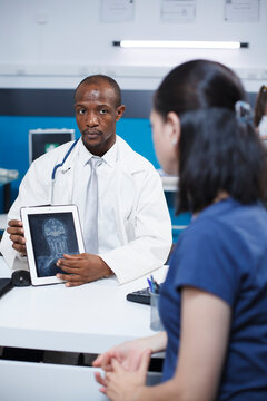African American doctor uses a tablet to diagnose cervical vertebra damage and neck pain of female patient. Black man medical examiner in a lab coat advising woman of best possible treatments.