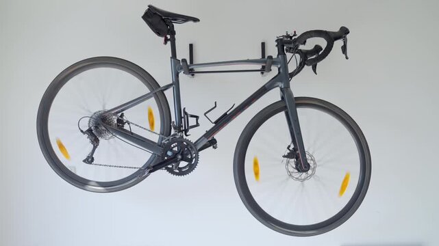 Bicycle hangs on wall mounted rack in garage. Road bike with spinning wheels against white wall. Concept of home bike storage and cycling equipment