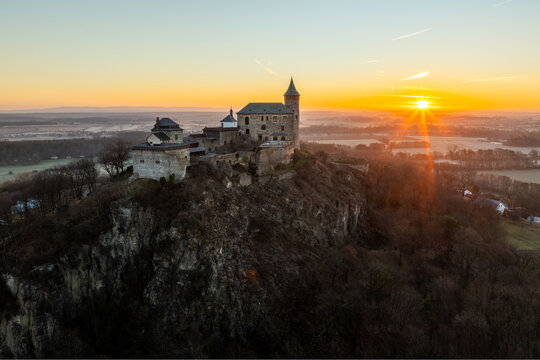 Aerial Drone Shot of Historic Kuneticka Hora Castle Silhouetted Against a Vibrant Sunrise Sky, Enveloped in Winter Morning Mist Over the castle and Surrounding Countryside, Pardubice Region, Kunětick&aacute;