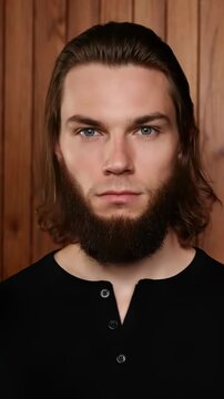 Young man poses for a portrait against a wooden background in a simple black shirt and casual style