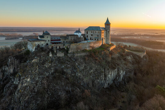 Aerial Drone Shot of Historic Kuneticka Hora Castle Silhouetted Against a Vibrant Sunrise Sky, Enveloped in Winter Morning Mist Over the castle and Surrounding Countryside, Pardubice Region, Kunětick&aacute;