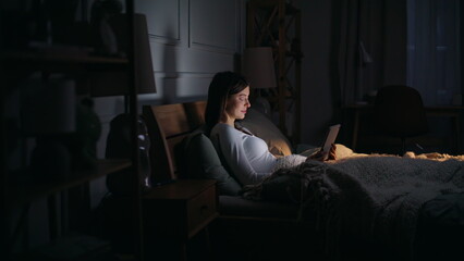 Fototapeta premium Lady surfing internet bedtime lying cozy dark bedroom. Freelancer reading email