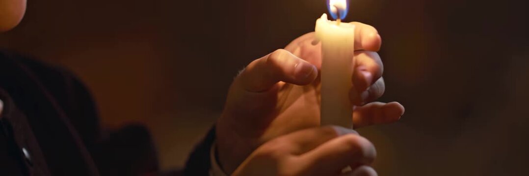 Hands holding burning candle creating warm spiritual moment during religious ritual, faith and devotion concept in wide banner format.