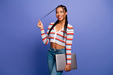 Young chic student woman with braids holding laptop and laughing against a blue background