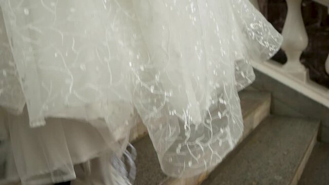 Low angle view of bride wearing white platform combat boots and shimmering lace wedding gown walking up classic marble staircase with white stone balustrade during ceremony preparation