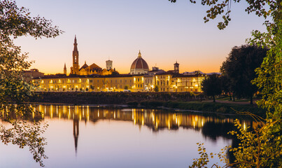 Obraz premium Florence skyline reflecting on Arno River during sunset, iconic Duomo and Ponte Vecchio illuminating historical cityscape