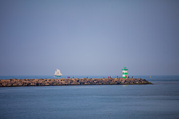 Sailboats drift peacefully near a green lighthouse along the serene coastline at sunset © Maksim Shebeko