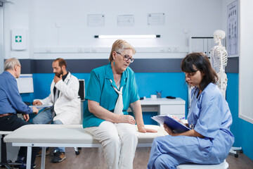 Obraz premium Elderly woman receives checkup from healthcare practitioner in blue scrubs. Retired senior patients in hospital room getting medical examinations from professional physiotherapists.
