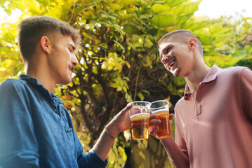 Fototapeta premium Two young men enjoying a vibrant outdoor gathering, smiling and raising plastic cups filled with golden beer, celebrating friendship and good times together