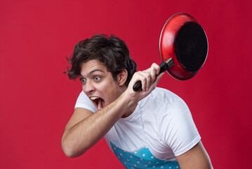 Man in playful pose holding a frying pan with an expressive face against a red background