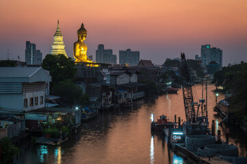Obraz premium Evening view of canal community in Bangkok, Thailand, with glowing giant Buddha statue