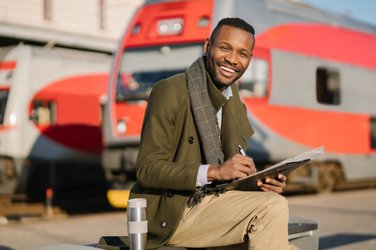Portrait of happy businessman with reusable cup and documents waiting for the train
