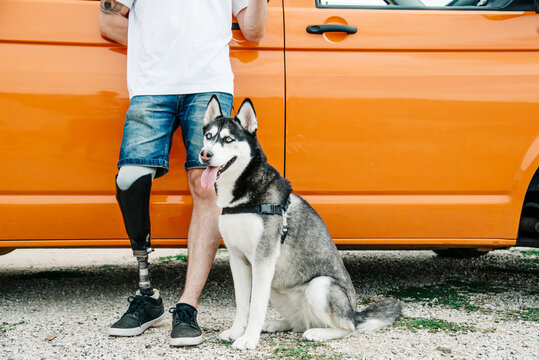 Young man with dog wearing leg prosthesis at camper van