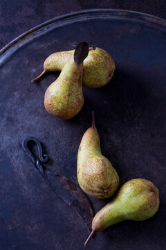 Four green pears 'Abate Fetel' and an old knife on rusty ground
