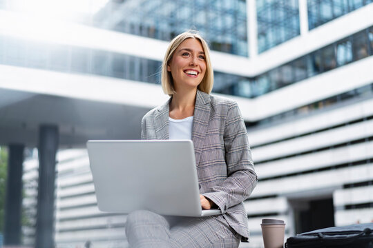 Smiling young businesswoman using laptop in the city
