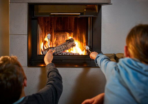 Back view of brother and sister with marshmallow Skewers in front of fire place
