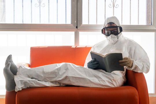 Woman in protective clothes, sitting on couch, reading book