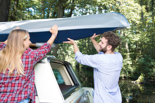 Smiling young couple taking canoe from car roof
