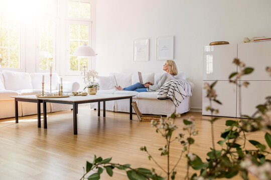 Blond mature woman sitting on couch in the living room using laptop
