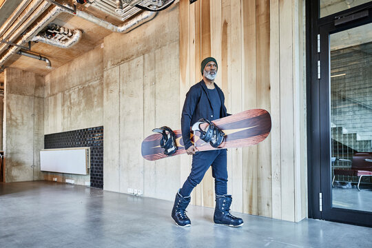 Mature businessman holding snowboard in modern office