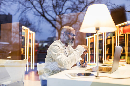 Mature man sitting at desk in a library in the evening using laptop