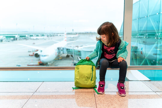 Girl with backpack sitting at the airport in front of a plane