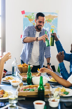 Group of friends clinking beer bottles at dining table