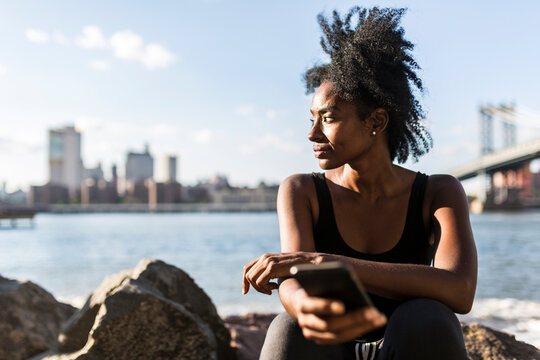 USA, New York City, Brooklyn, woman with cell phone sitting at the waterfront